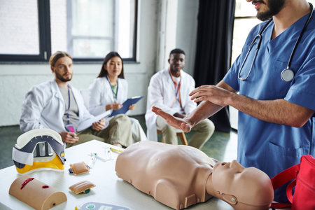 healthcare worker showing life-saving techniques on CPR manikin near medical equipment and diverse group of interracial students on blurred background, acquiring life-saving skills conceptの写真素材