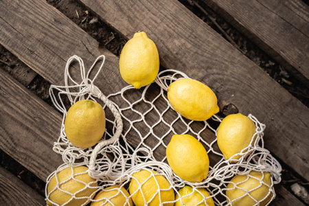 Top view of fresh and juicy lemons lying near mesh bag on wooden planks, yellow fruit, citrus, composition, ingredients, rustic, sour food, vitamin c, summer conceptの写真素材