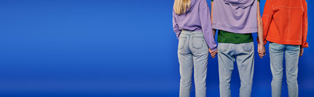 polygamy, back view of polyamory three people, young man and women holding hands on blue background, studio shot, denim fashion, love triangle, cropped shot, bonding, bannerの写真素材