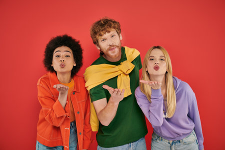 open relationship, polygamy concept, three interracial lovers blowing air kiss on coral background,...