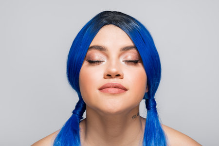 modern subculture, tattooed woman with closed eyes and blue hair posing on grey background, hairstyle, vibrant color, modern beauty, self expression, individualismの写真素材