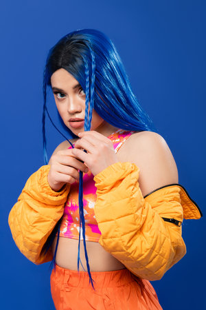 colorful clothes, young woman with dyed hair posing in puffer jacket on blue background, vibrant...