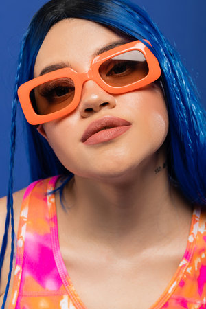 portrait, trendy accessory, young female model with blue hair and trendy sunglasses isolated on blue background, generation z, rebel style, rebel style, individualism, modern womanの写真素材