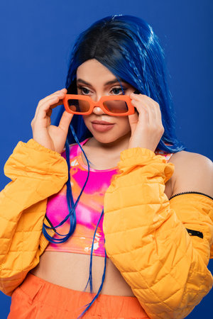 fashion and style, young female model with blue hair and braids wearing orange sunglasses isolated...