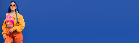 gen z, fashion statement, female model with blue hair adjusting trendy sunglasses isolated on blue...