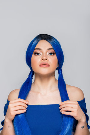beauty trends, dyed hair, female model looking at camera, portrait of tattooed woman with bare shoulders posing in bright blouse on grey background, blue hair color, hairstyle, makeup and beautyの写真素材