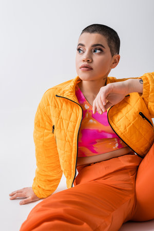 outerwear, fashion statement, tattooed young woman in colorful clothes sitting and looking away on...