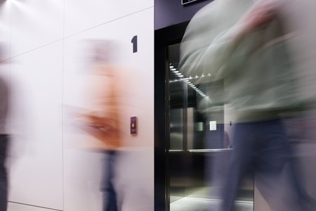 long exposure of business people walking near elevator with open doors in contemporary coworking office with high tech interior, movement, dynamic business, productivityの写真素材