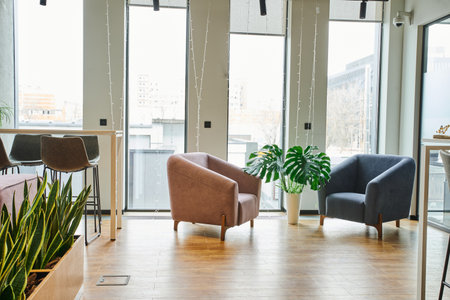 spacious office lounge with large windows, cozy and comfortable armchairs, green and natural plants in modern coworking environment, workspace organization conceptの写真素材