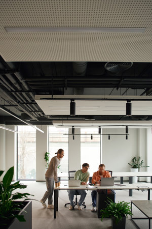 team lead in casual clothes standing near colleagues working on startup project near laptops in...
