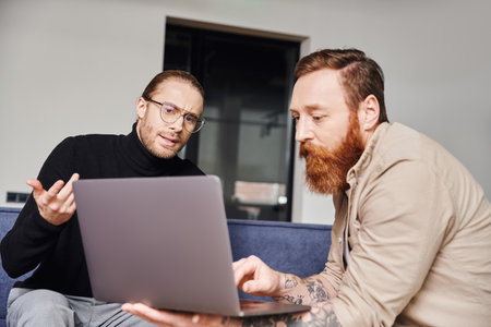 businessman in black turtleneck and eyeglasses gesturing while talking to bearded tattooed...