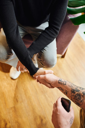 top view of entrepreneur in black turtleneck shaking hands with tattooed businessman with mobile phone, cropped view, successful partnership conceptの写真素材