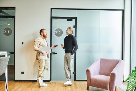 full length of stylish business colleagues with laptop and mobile phones standing in lobby of modern coworking space and planning startup project, productivity and cooperation conceptの写真素材
