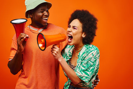 Cheerful young african american man in summer outfit and panama hat looking at stylish best friend...