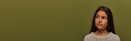 Portrait of pensive preteen brunette girl in trendy knitted sweater looking away while standing isolated on green with copy space, stylish girl in cozy fall attire concept, bannerの写真素材