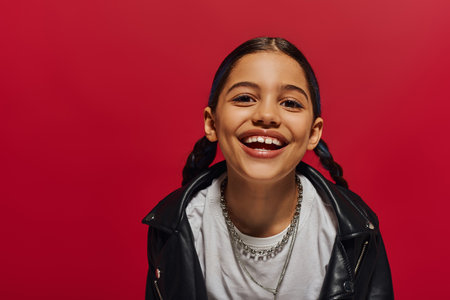 Portrait of pleased preadolescent girl with hairstyle wearing stylish leather jacket and looking at...