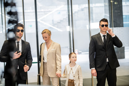personal security concept, two bodyguards in suits and sunglasses protecting happy mother and child...