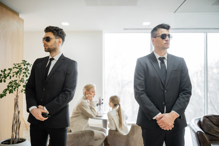 private security service, personal safety concept, handsome bodyguards in formal wear and sunglasses protecting safety of clients on blurred background, mother and daughter in cafeの写真素材
