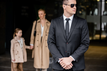 personal security service, lifestyle, bodyguard in suit standing near successful woman with preteen...