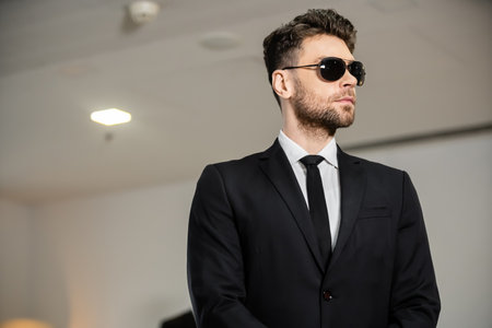 professional headshots, bodyguard service, handsome man in sunglasses and black suit with tie, hotel safety, security management, surveillance and vigilance, uniformed guard on duty looking awayの写真素材