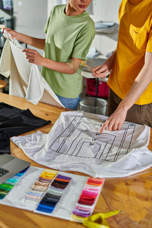 Cropped view of craftsman holding printing sample and pointing at t-shirt while working with african...