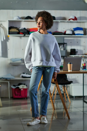 Full length of young african american craftswoman in sweatshirt and jeans looking away while...