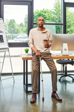 inclusion, myasthenia gravis syndrome, bold african american man standing with walking cane and coffee to go, computer monitor, dark skinned office worker in smart casual attireの写真素材