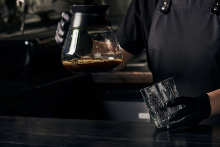 barista in black gloves holding glass and coffee pot of freshly brewed aromatic espressoの写真素材