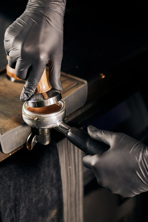 cropped view of barista in black latex gloves pressing ground coffee in portafilterの写真素材