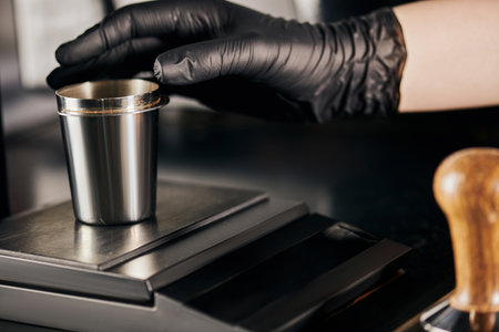 partial view, professional barista in black latex glove taking metallic measuring cup in coffee shopの写真素材