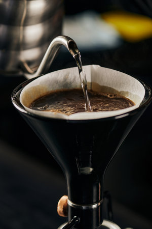 boiling water pouring from kettle into siphon coffee maker with paper filter and coffee with foamの写真素材