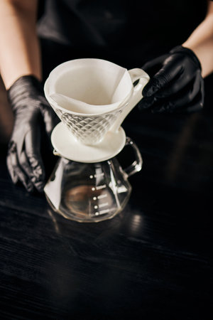barista in black latex gloves near ceramic dripper and glass pot, V-60 style espresso brewing methodの写真素材