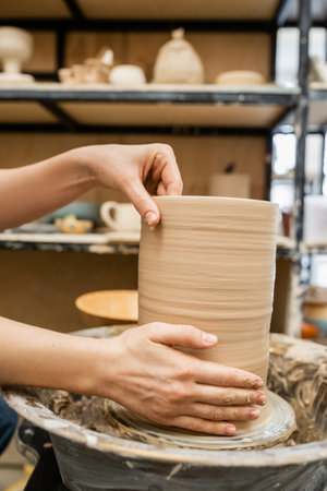 Cropped view of hands of craftswoman making clay vase on pottery wheel in workshopの写真素材