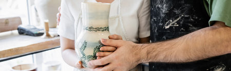 Cropped view of couple of artisans in aprons holding clay vase in ceramic workshop, bannerの写真素材