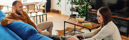 Smiling woman petting border collie dog on couch near boyfriend in living room, bannerの写真素材