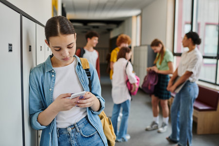 teenage girl texting on smartphone in school hallway, students and teacher on blurred backgroundの写真素材