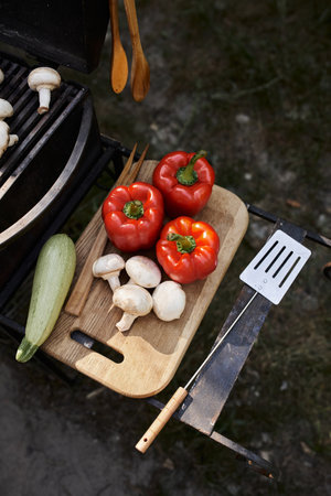 Top view of fresh vegetables on cutting board near barbecue during picnic outdoors, food and natureの写真素材