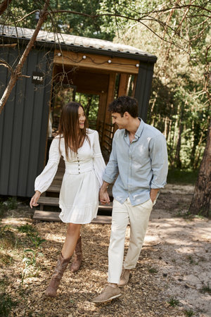 positive man and woman holding hands and walking together near  summer house, vacation, romanceの写真素材