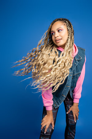 charming african american woman with dreadlocks and long hair posing on blue background in studio