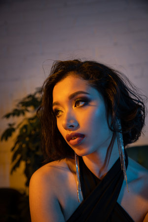 Confident young asian woman with evening visage spending time in night club with evening