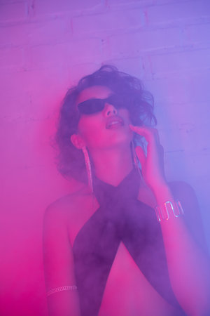 Sexy young asian woman in sunglasses posing in smoke and neon lighting in night club