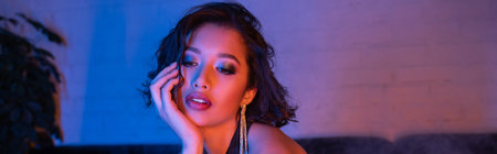 Trendy young asian woman with makeup and hairstyle standing in neon light in night club, banner