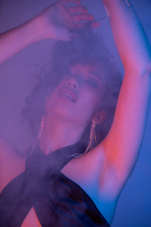 Trendy young brunette asian woman dancing in smoke and neon lighting in night club