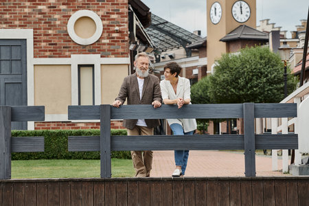 happy elderly couple, woman looking at man, standing near fence, urban backdrop, aging populationの写真素材