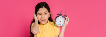 schoolgirl looking at camera, winking, holding alarm clock isolated on pink, back to school, bannerの写真素材