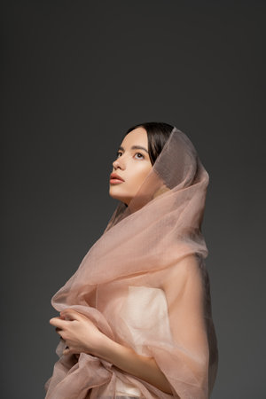 Pretty young asian model with everyday makeup and beige cloth posing isolated on greyの写真素材