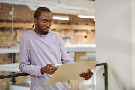 african american man looking at project on paper, using smartphone, planning, strategy, digital