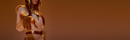 Cropped view of woman in egyptian attire pointing with finger and posing on brown background, banner