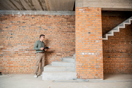 full length of property broker with folder standing near stairs in cottage with unfinished interiorの写真素材