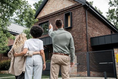back view of real estate broker showing new cottage to interracial lesbian couple outdoorsの写真素材